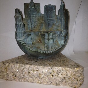 May include: A bronze sculpture of a city skyline, with buildings and streets, inside a hollowed-out sphere. The sculpture is sitting on a granite base.