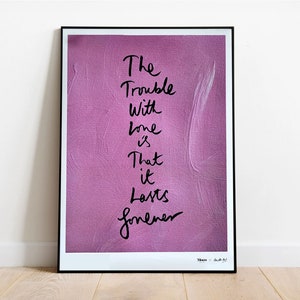 May include: A framed print with a pink background and black text that reads "The Trouble With Love Is That It Lasts Forever". The text is written in a handwritten style. The print is framed in a black frame.