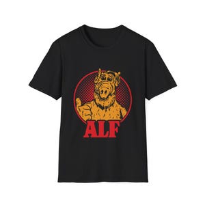 May include: Black t-shirt with a red circle graphic featuring ALF, a furry alien character with big eyes and a thumbs up, and the word "ALF" in red letters below.