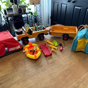 May include: A vintage Fisher-Price Adventure People toy set. The set includes a red tent, a yellow jeep with figures, a trailer, a raft, a red slide, and other accessories. The tent is red with a black base.