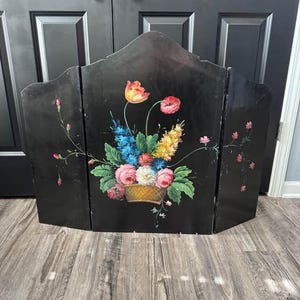 May include: A black, three-panel folding screen with a hand-painted floral design. The flowers include pink roses, blue delphiniums, yellow blossoms, and a large orange tulip. The screen is made of wood and has a decorative, arched top.