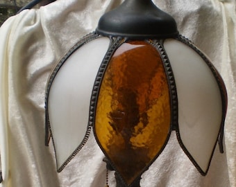 May include: A vintage table lamp with a white and amber glass shade. The lamp has a black metal base with a decorative design.