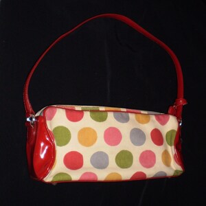 May include: A red and white polka dot handbag with a red leather strap. The bag has a zip closure and a small pocket on the front.