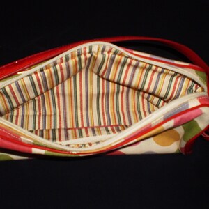 May include: A red and white polka dot handbag with a striped fabric lining. The bag has a red patent leather trim and a red leather strap.