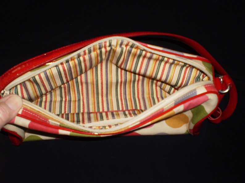 May include: A red and white polka dot handbag with a striped fabric lining. The bag has a red patent leather trim and a red leather strap.