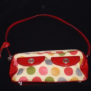 May include: A red and white polka dot handbag with a red leather trim and a heart-shaped charm. The bag has two pockets on the front.
