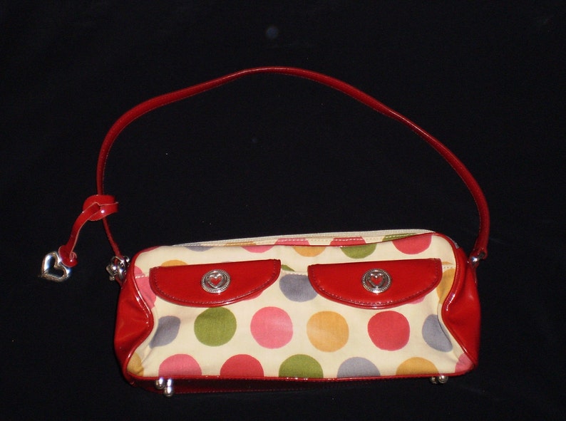May include: A red and white polka dot handbag with a red leather trim and a heart-shaped charm. The bag has two pockets on the front.