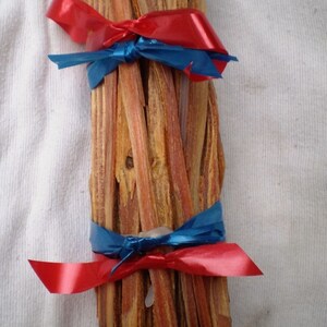 May include: A bundle of thin, brown sticks tied together with red and blue ribbon. The sticks are arranged in a vertical stack and are tied at the top and bottom with the ribbon.
