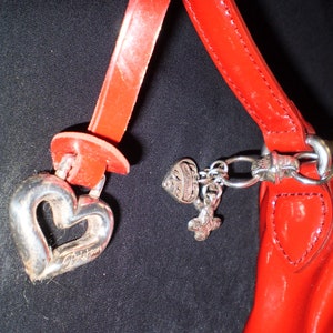May include: A red leather handbag with a silver heart charm and other silver charms. The bag has a top handle and a shoulder strap.