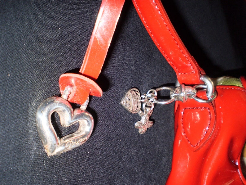 May include: A red leather handbag with a silver heart charm and other silver charms. The bag has a top handle and a shoulder strap.