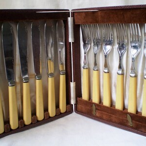May include: A set of eight silver-plated knives and forks with ivory-colored handles, in a brown leather case.