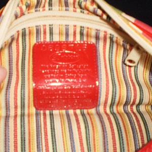 May include: The inside of a red and white striped handbag with a red leather tag that says "Guess?" in white letters.