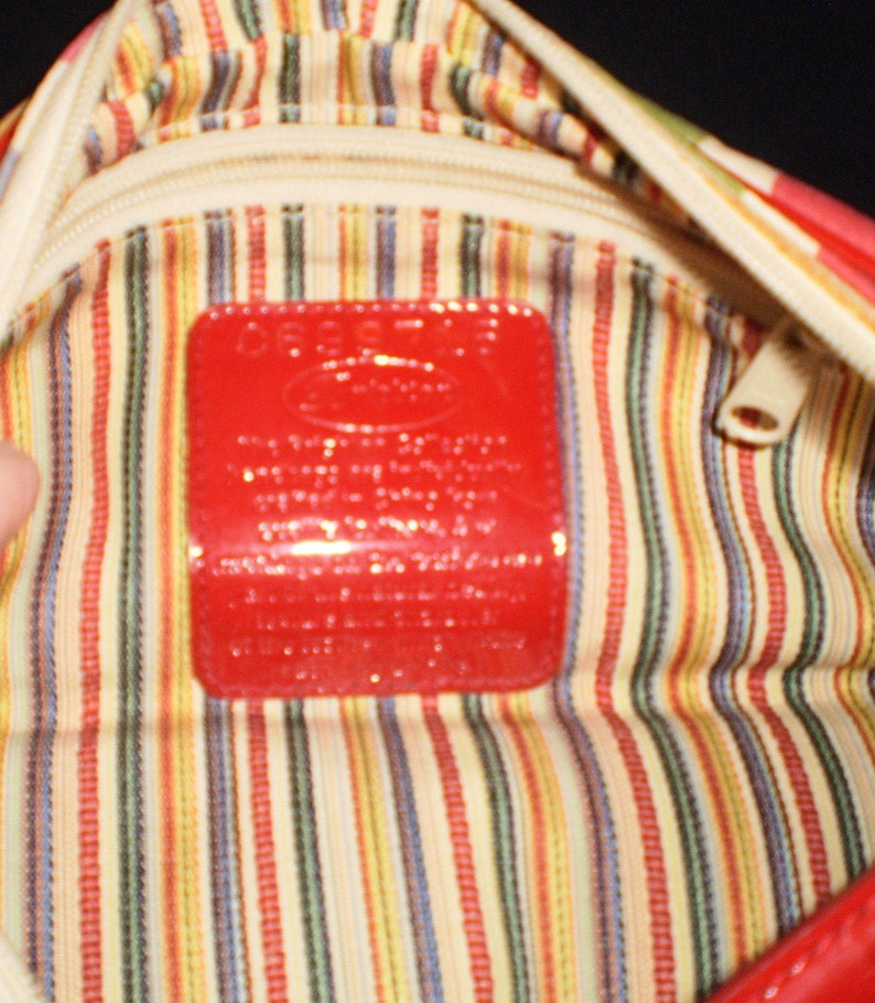 May include: The inside of a red and white striped handbag with a red leather tag that says "Guess?" in white letters.