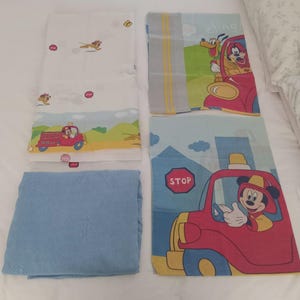 May include: A set of four bedding pieces featuring Disney characters. One white sheet has small cartoon figures and a red fire truck. One blue sheet is solid. Two pillowcases display a red fire truck, a stop sign, and cartoon characters.
