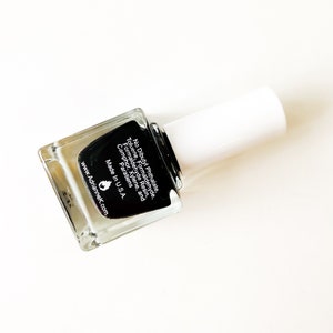 May include: A clear glass bottle of black nail polish with a white cap. The bottle label lists ingredients and states "No Dibutyl Phthalate, Toluene, Formaldehyde, Formaldehyde Resin, Camphor, Xylene, and Parabens. Made in U.S.A. www.Adriannek.com"
