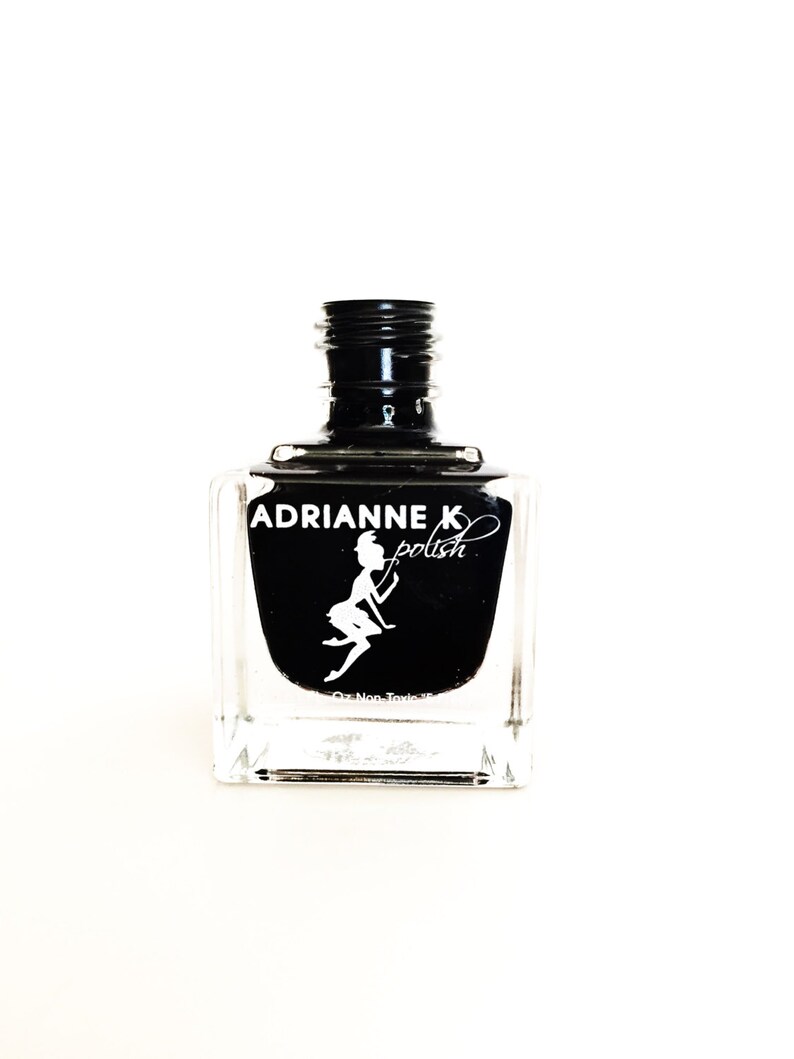 May include: A black nail polish bottle with a clear glass bottle and a black cap. The bottle has a white label with the text "ADRIANNE K polish" and a silhouette of a fairy.