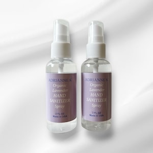 Könnte beinhalten: Zwei durchsichtige Plastikflaschen mit Bio-Lavendel-Handdesinfektionsspray. Jede Flasche ist mit "ADRIANNE K Bio-Lavendel Handdesinfektionsspray" und "2 FL OZ Hergestellt in den USA" beschriftet.