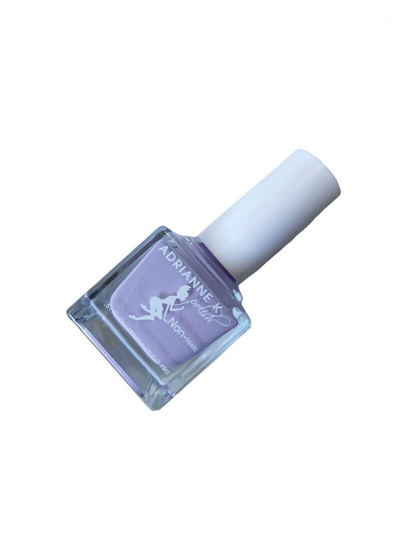 Peut inclure: Un flacon carr&eacute; de vernis &agrave; ongles violet clair avec un bouchon blanc. Le flacon porte une &eacute;tiquette indiquant "Adrianne K polish" et "Non-toxique".