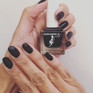 May include: A black nail polish bottle with the brand name "Adrianne K polish" and a fairy illustration. The bottle is being held by a hand with black nail polish.