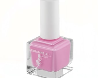 Può includere: Un flacone quadrato di smalto per unghie rosa con un tappo bianco. Il flacone ha un'etichetta con la scritta "Adrianne K polish" e una piccola illustrazione di una donna con un vestito.