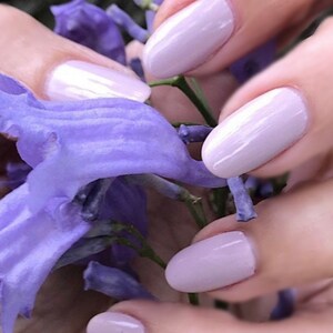 Peut inclure: Gros plan sur des mains avec un vernis &agrave; ongles violet clair, tenant un bouquet de fleurs violettes.