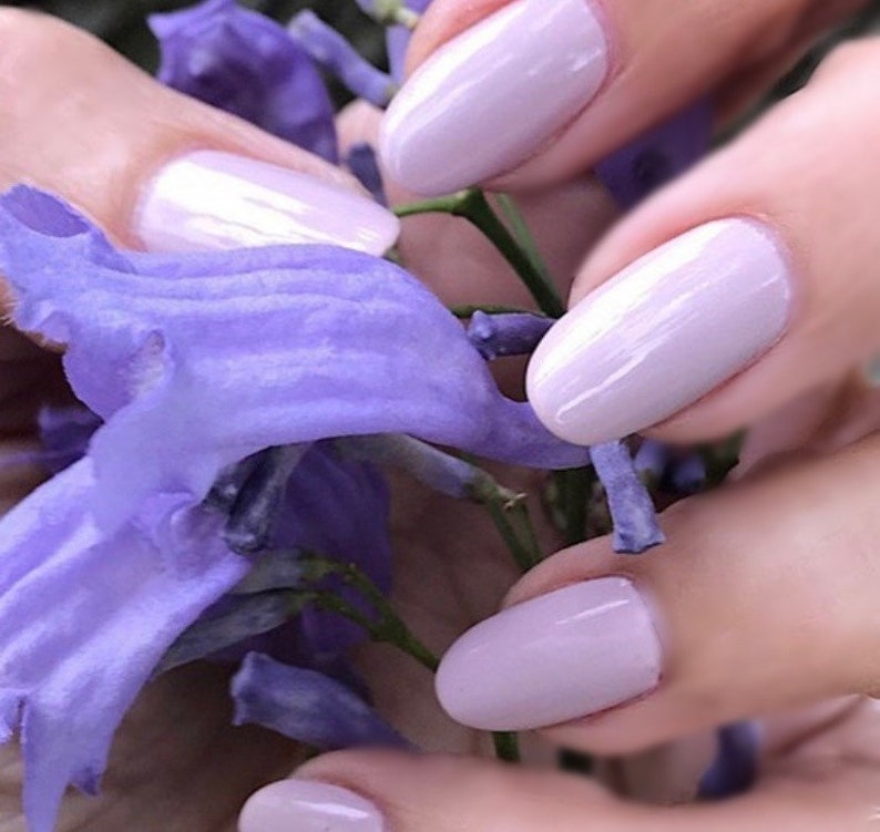 Peut inclure: Gros plan sur des mains avec un vernis &agrave; ongles violet clair, tenant un bouquet de fleurs violettes.