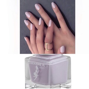 Peut inclure: Un flacon de vernis &agrave; ongles de couleur lilas clair avec le nom de la marque "Drianne K Polish" sur l'&eacute;tiquette. Le flacon est de forme carr&eacute;e et poss&egrave;de un bouchon en verre transparent.
