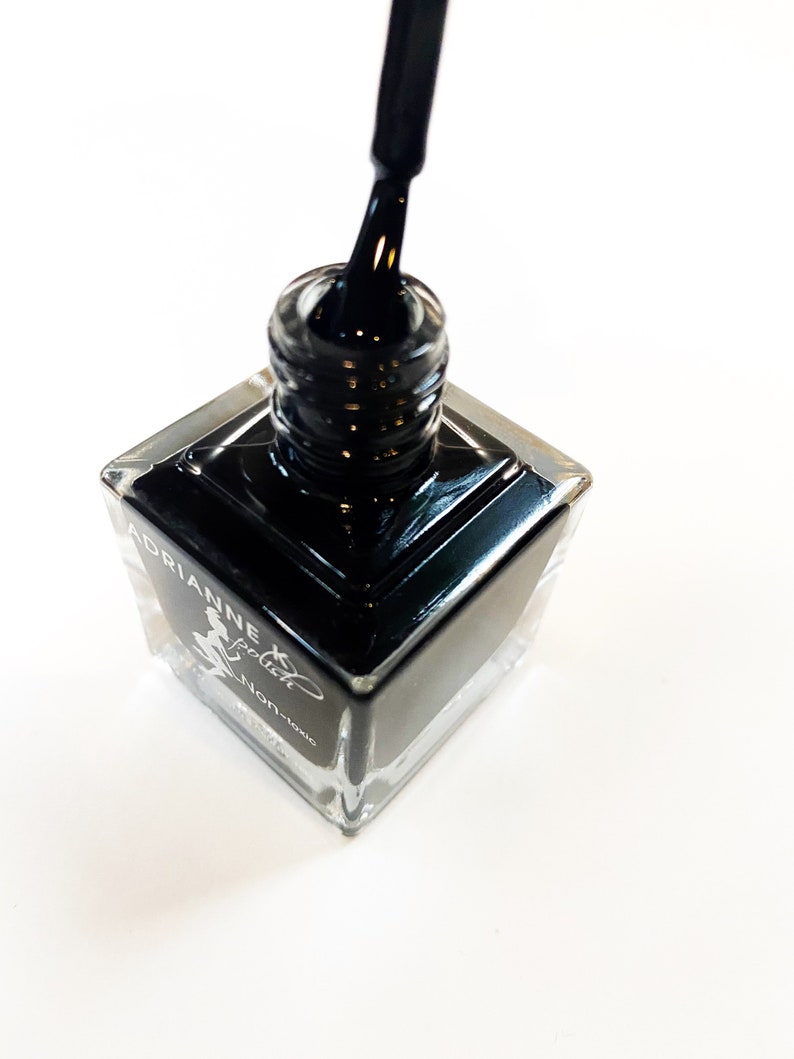 May include: A square bottle of black nail polish with a silver cap and a black brush. The bottle is labeled "Adrianne Special Non-toxic".