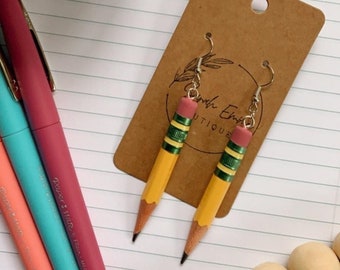 May include: A pair of yellow pencil earrings with green and pink details. The earrings are on a brown card with the text "Smith Ellis Boutique".