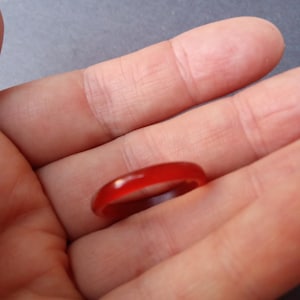May include: A simple red ring made of smooth, polished material. The ring is thin and has a rounded shape.
