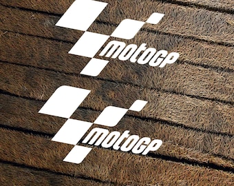 May include: Two white vinyl stickers with a checkered flag design and the word "motogp" printed on them. The stickers are on a brown textured background.