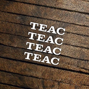 以下が含まれることがあります： 茶色のテクスチャの背景に、白い文字で「TEAC」という単語が4回繰り返されています。