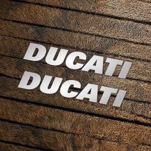 May include: The word "DUCATI" is written twice in white letters on a brown, textured background.