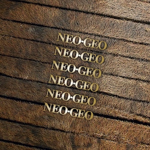 Op de afbeelding: Een close-up van een houten oppervlak met de tekst "NEO-GEO" zes keer herhaald in gouden letters.