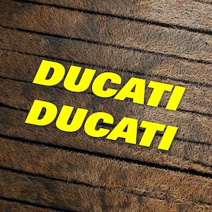 May include: The word "DUCATI" is written twice in yellow letters on a brown, textured background.