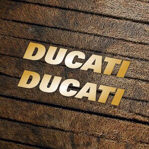 May include: The word "DUCATI" is written twice in gold letters on a brown, textured background.