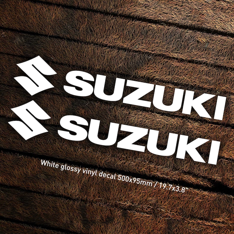 May include: Two white vinyl decals with the word "SUZUKI" in bold white letters. The decals are on a brown woodgrain background. White glossy vinyl decal 500x95mm / 19.7x3.8"