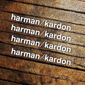 May include: A textured brown surface with a fibrous, grass-like appearance composed of parallel horizontal lines. The white text "harman/kardon" is repeated four times in a vertical column, centered across the brown, coarse-textured background.