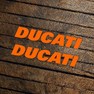 May include: The word "DUCATI" is written twice in orange letters on a brown, textured background.