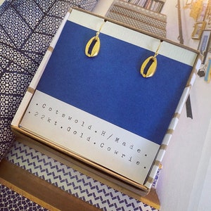 May include: A pair of gold cowrie shell earrings in a blue box with the text "Cotswold. H/Made. 22kt. Gold. Cowrie."
