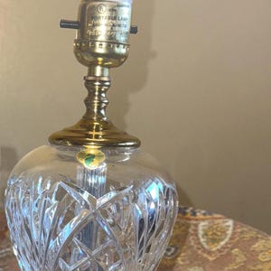 May include: A crystal table lamp with a cut glass shade and a brass base. The lamp has a white LED bulb and a label that reads "CAUTION: RISK OF FIRE MAX 75 WATT TYPE A LAMP(S)".