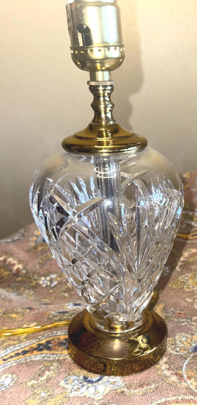 May include: A clear crystal table lamp with a gold-colored base and accents. The lamp features a cut glass design on the bulbous body and a brass-colored top. The lamp is designed for indoor use.