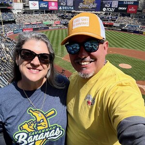 Puede incluir: Una foto de dos personas en un partido de b&eacute;isbol. Una persona lleva una camiseta amarilla y una gorra amarilla con el texto "THIS SHIT IS BANANAS". La otra persona lleva una camiseta azul con el logo de Savannah Bananas.
