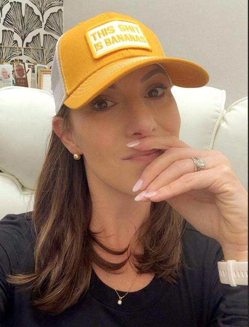 Puede incluir: Gorra de b&eacute;isbol de color amarillo mostaza con la parte trasera de malla blanca. La gorra presenta el texto "THIS SHIT IS BANANAS" en un parche rectangular. La persona de la imagen lleva una camiseta negra y un collar dorado.