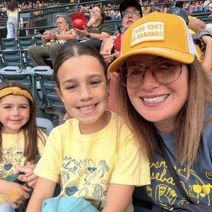 Puede incluir: Tres personas sonriendo en un partido de b&eacute;isbol. La mujer de enfrente lleva un sombrero amarillo con el texto "THIS SHIT IS BANANAS". Los dos ni&ntilde;os llevan camisetas amarillas con un dise&ntilde;o de b&eacute;isbol.