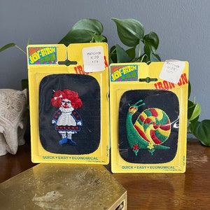 May include: Two vintage iron-on patches on yellow backing. One features a doll with red hair and a blue dress. The other shows a snail with a colorful shell. Both patches are on a black background and are labeled "Joy-Patch".