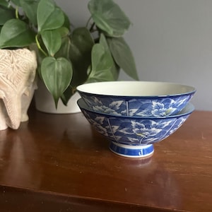 May include: Two blue and white porcelain bowls with a floral design. The bowls are stacked on top of each other and have a small foot.