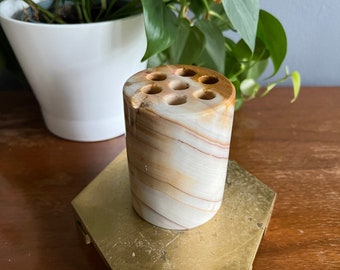 May include: A white and brown marble pencil holder with eight holes. The holder is sitting on a gold metal stand.