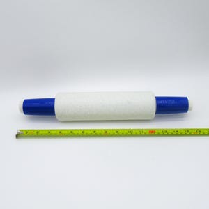 May include: A paint roller with a white, textured roller and blue handles. The roller is approximately 7 inches long, with a total length of 10 inches including the handles. A yellow measuring tape is in the foreground.