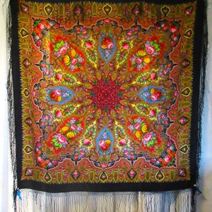 May include: A square black shawl featuring a vibrant, symmetrical floral pattern in shades of red, yellow, pink, blue, and green. The design radiates from a central red floral motif, surrounded by intricate paisley and leaf details with black fringe.
